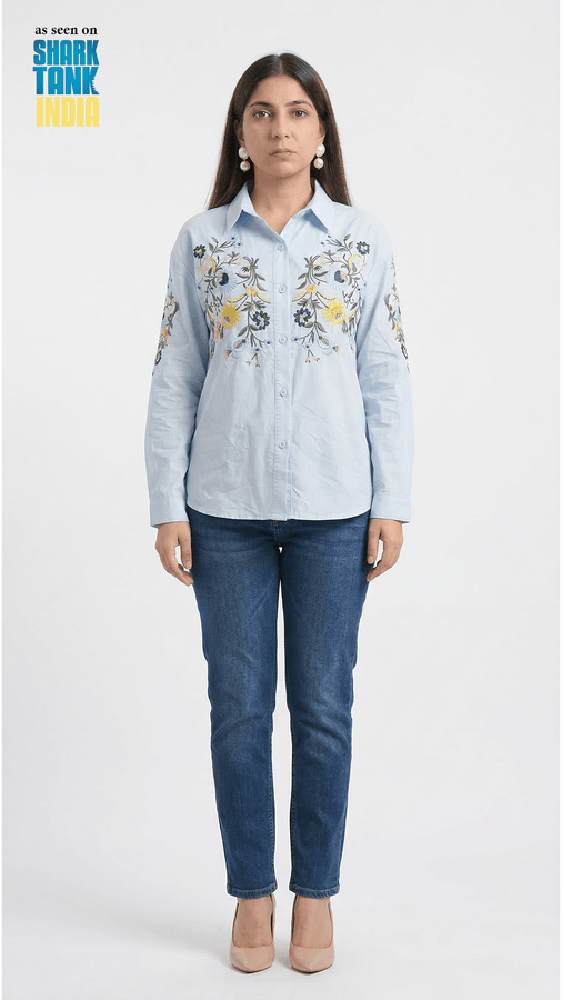 Woman wearing a light blue embroidered shirt and dark blue jeans on a white background