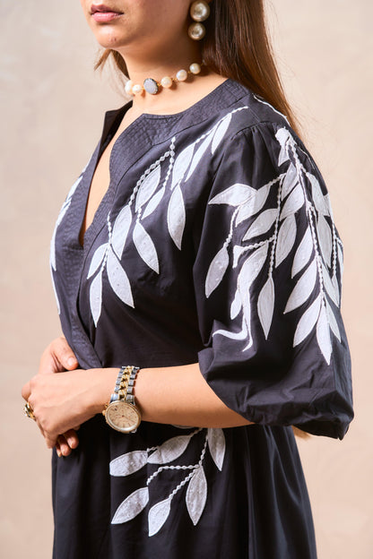 Black dress with white leaf patterns worn by a person, against a neutral background