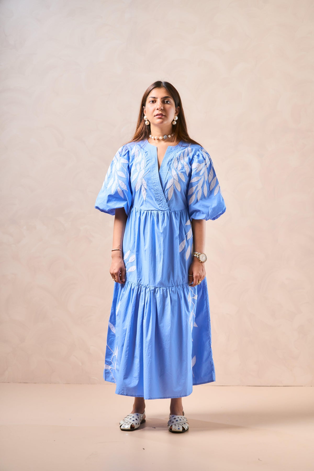Woman wearing a blue dress with white patterns against a beige background