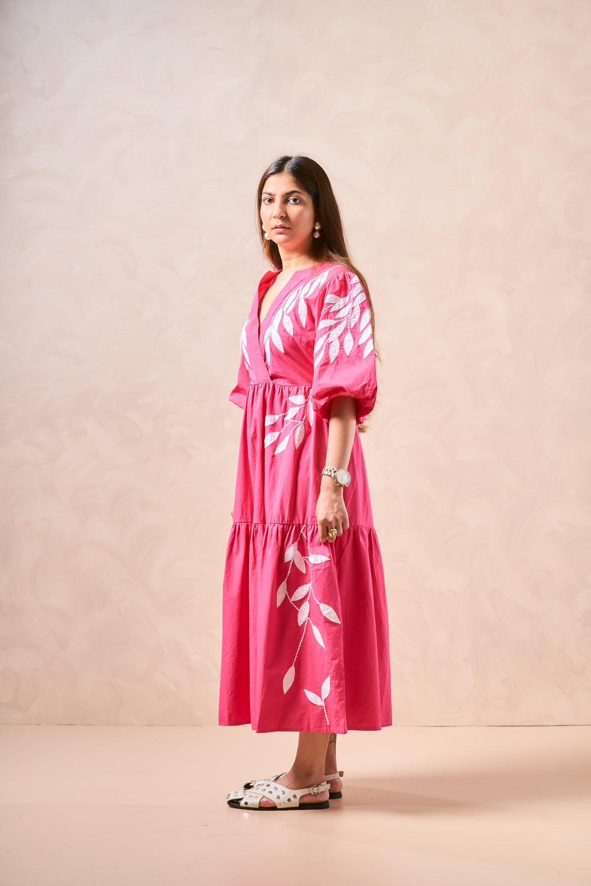 Woman wearing a pink dress with white floral patterns against a beige background
