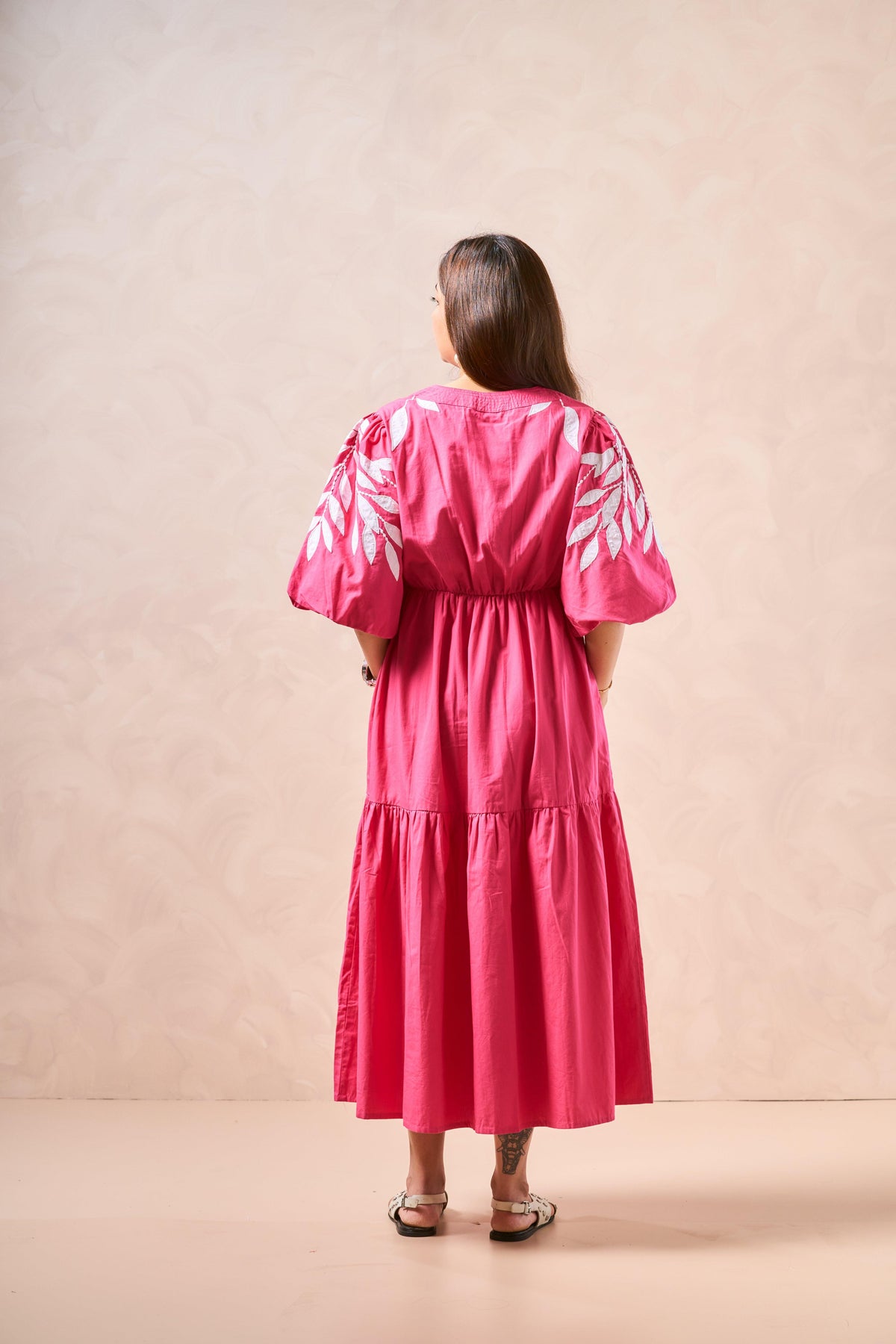Woman wearing a pink dress with leaf patterns on a beige background