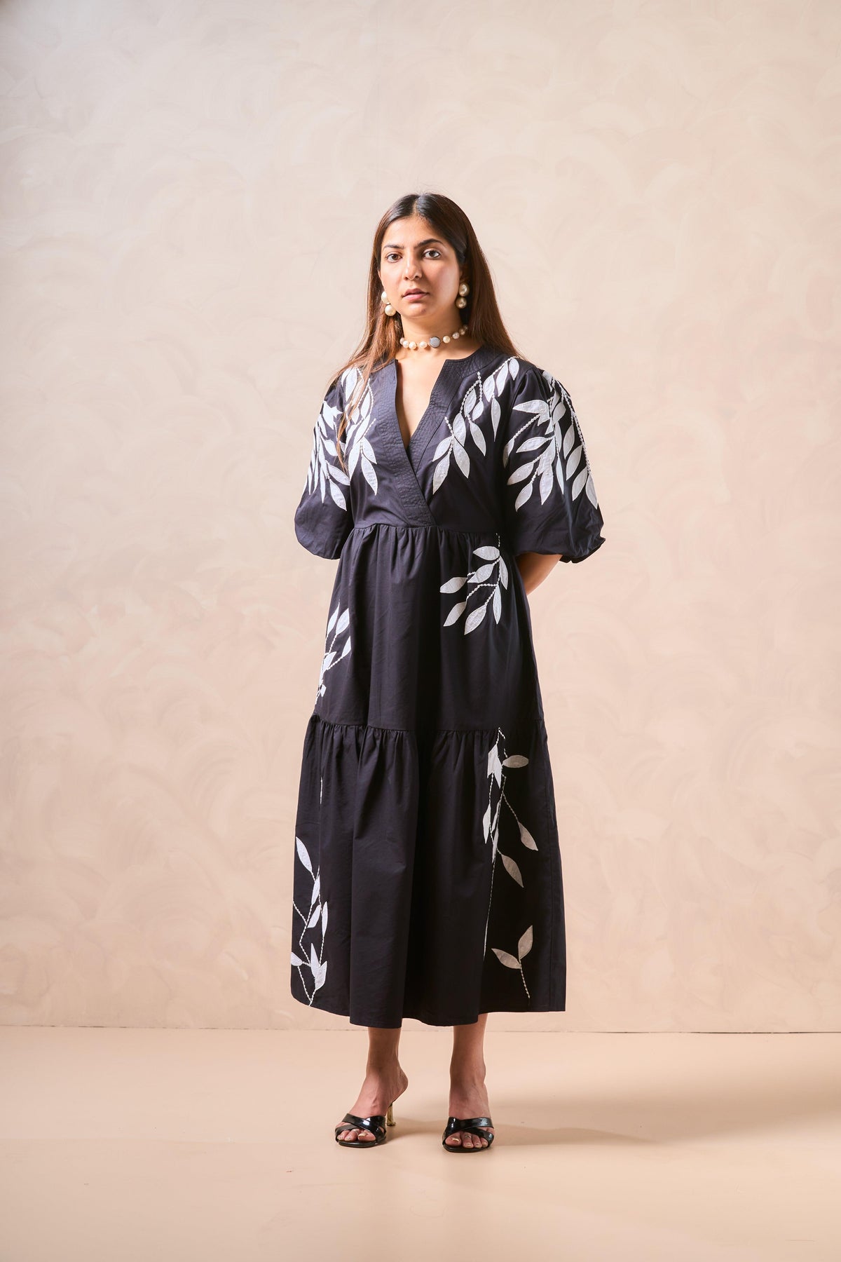 Woman wearing a black dress with white floral patterns against a beige background