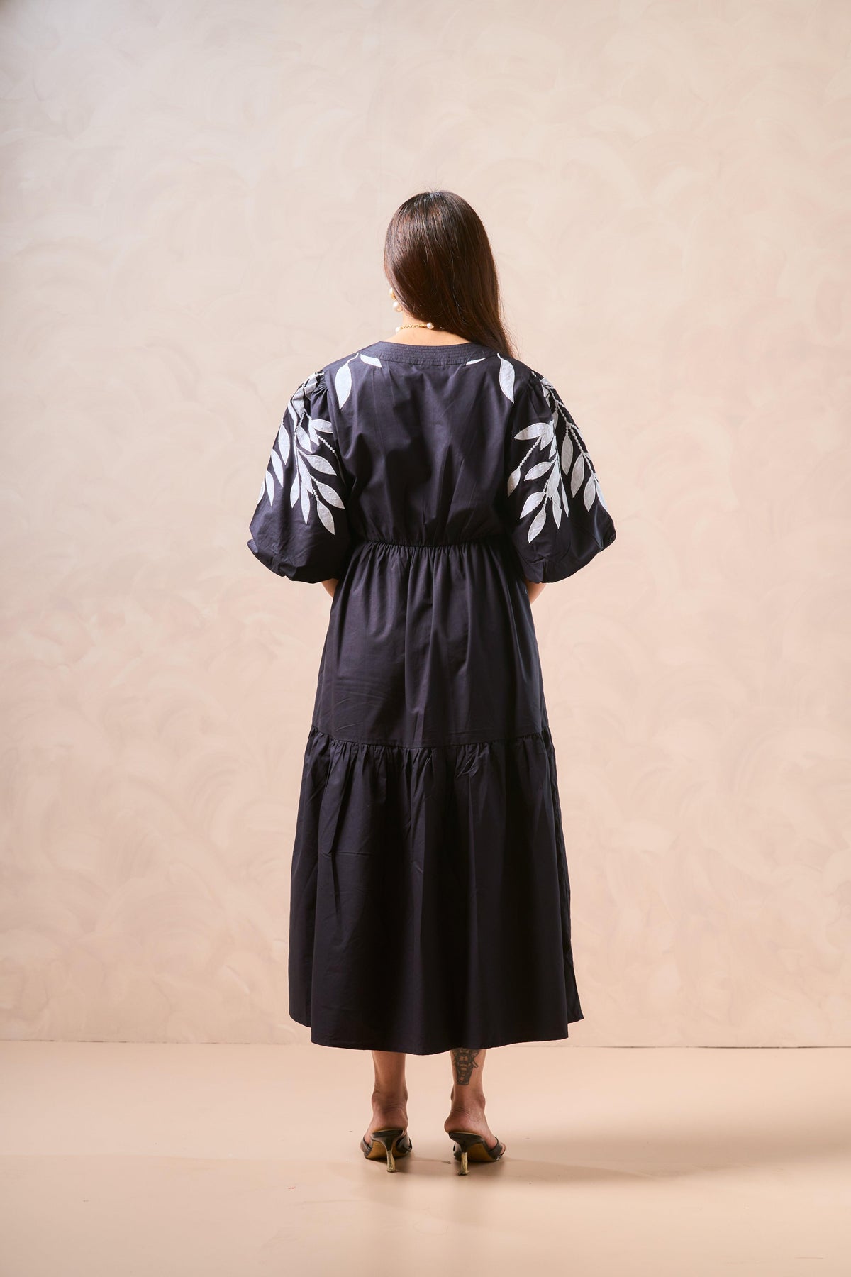 Woman wearing a black dress with white patterns standing against a beige background