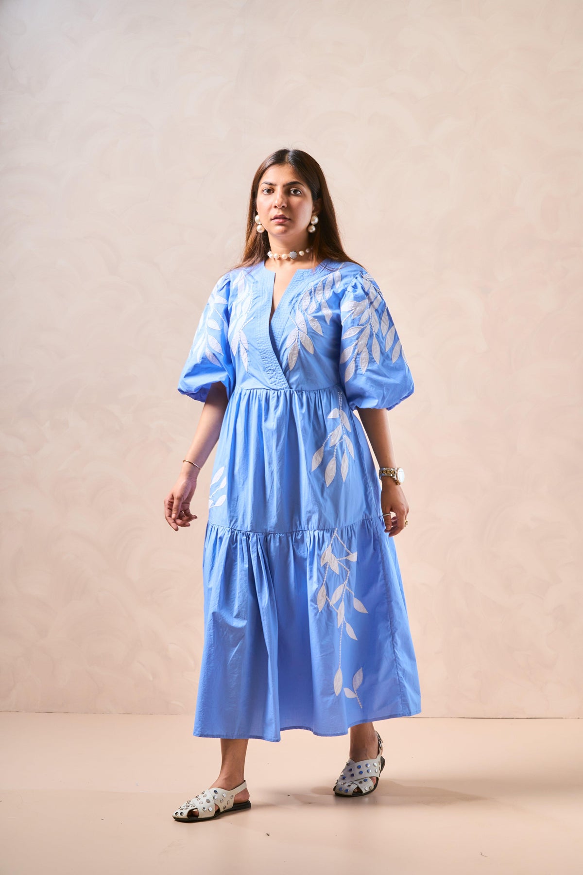 Woman wearing a blue dress with white patterns against a beige background