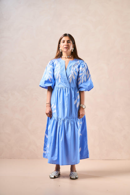 Woman wearing a blue dress with white patterns against a beige background