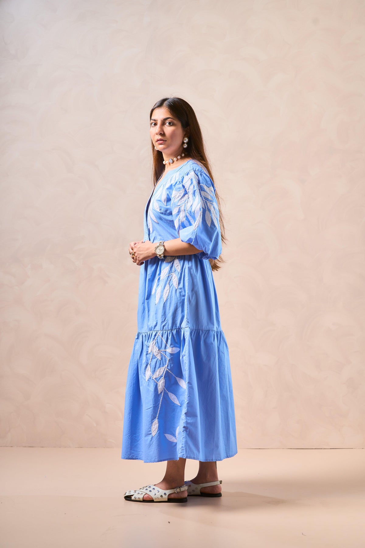 Woman wearing a blue dress with white floral embroidery against a beige background