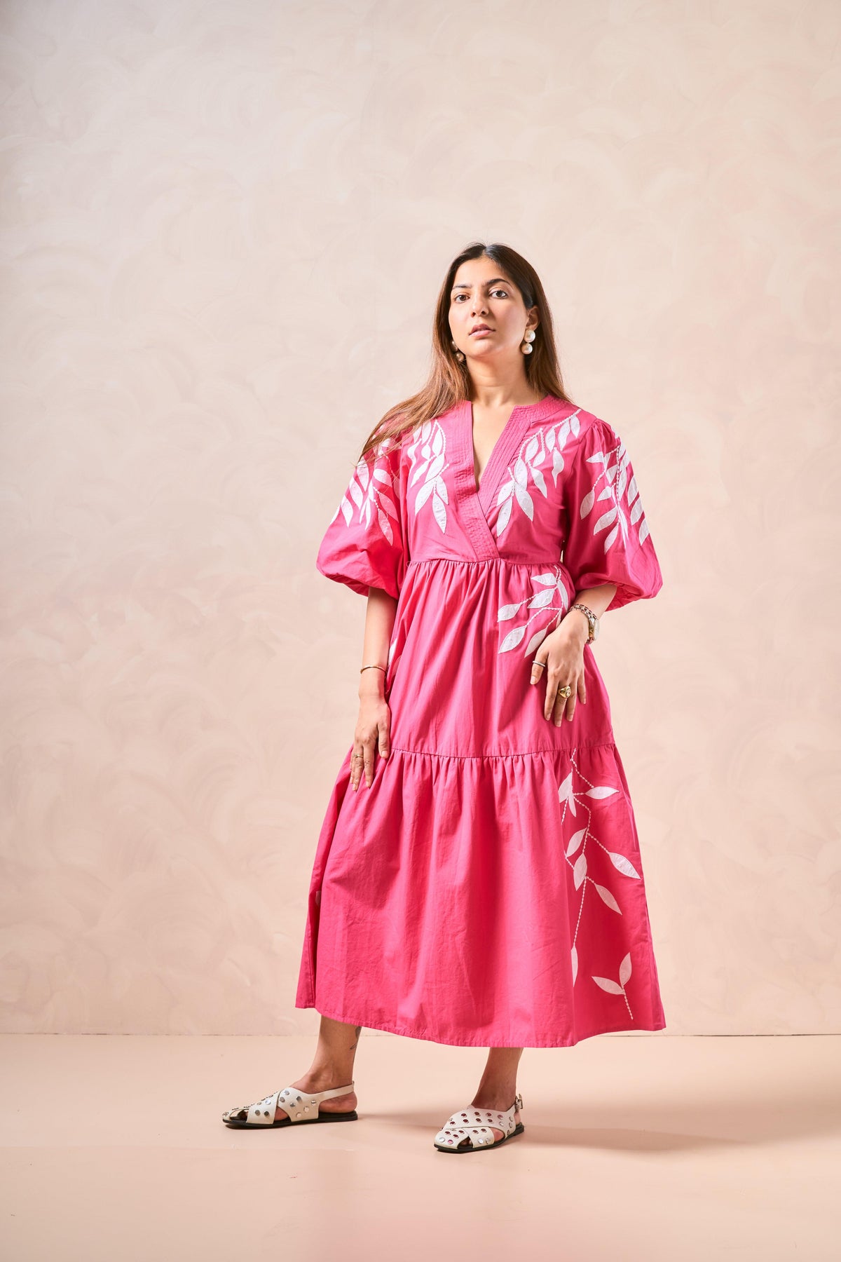 Woman wearing a pink dress with white floral patterns against a beige background
