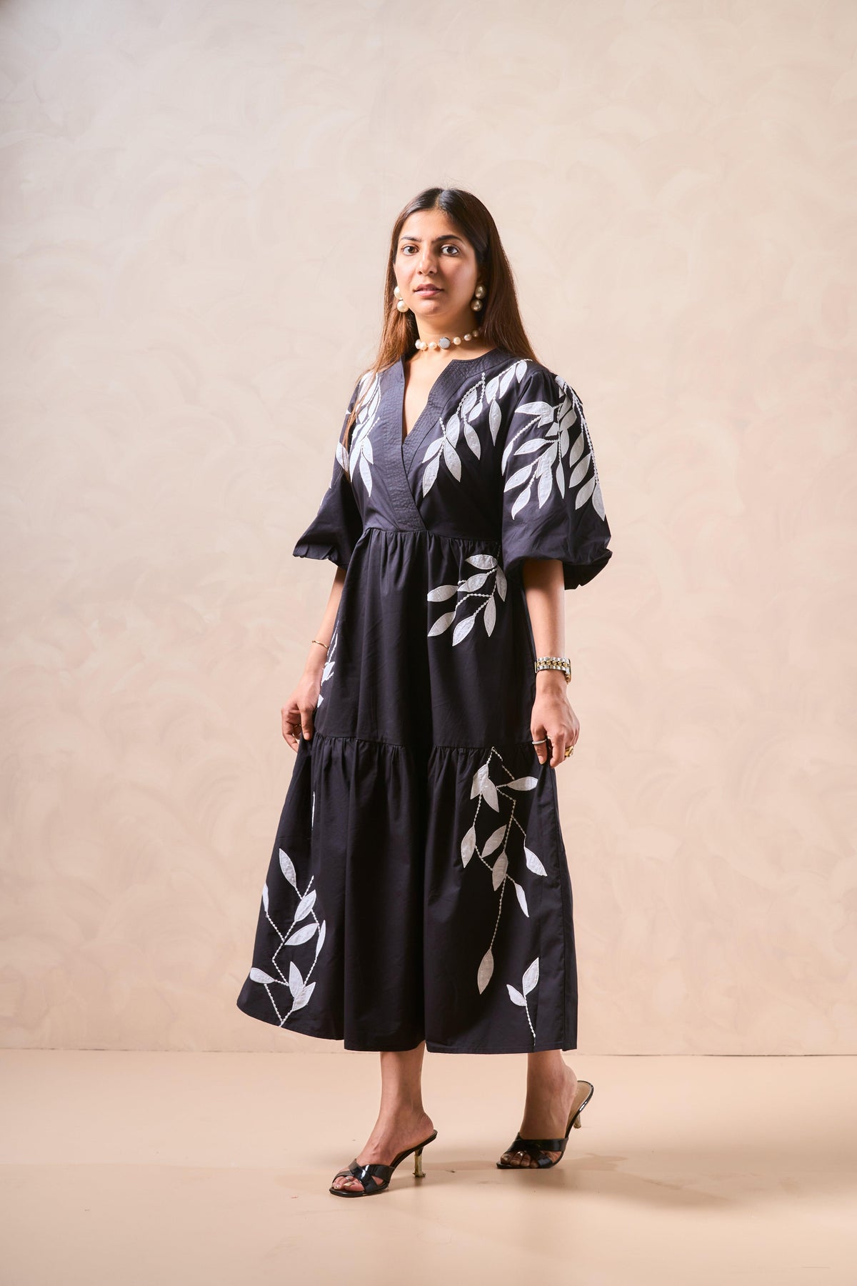 Woman wearing a black dress with white floral patterns against a beige background