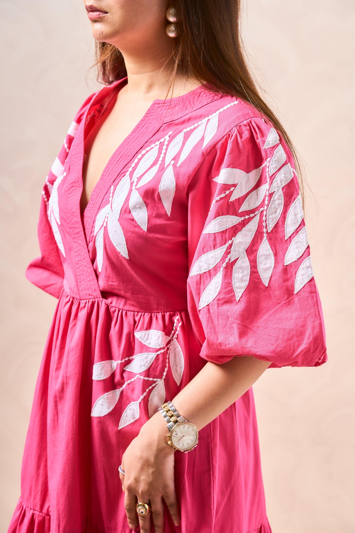 Woman wearing a pink dress with white leaf patterns on a beige background