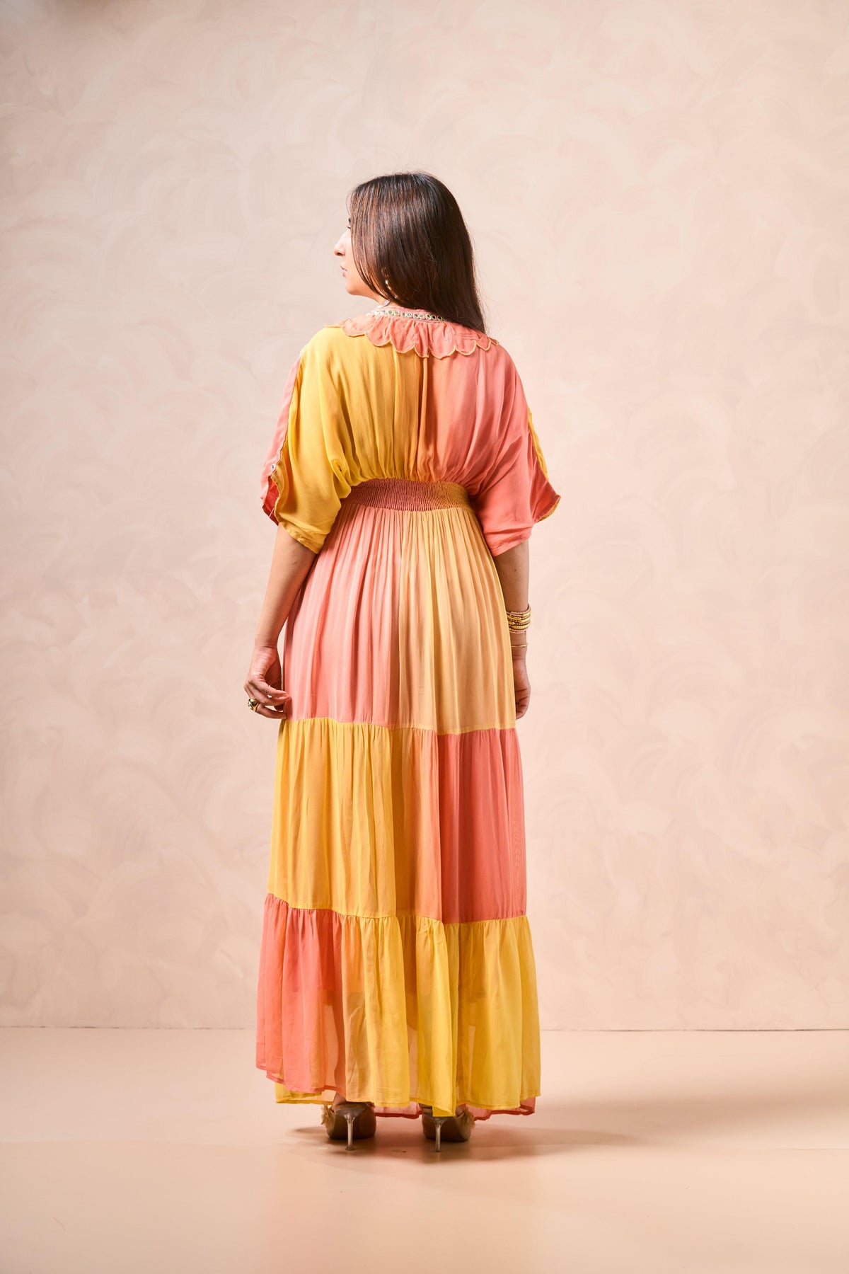 Woman wearing a colorful dress with a pink and yellow pattern against a beige background