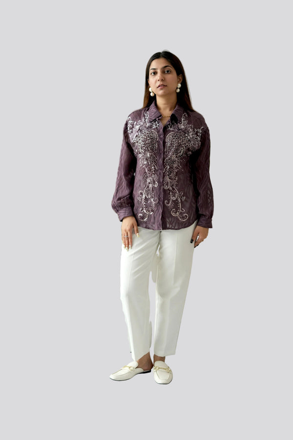 Woman wearing a patterned shirt and white pants on a plain background