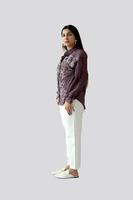 Woman wearing a patterned shirt and white pants on a plain background