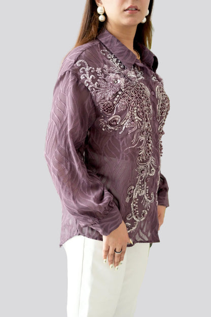 Woman wearing a purple embroidered blouse with white pants on a light gray background