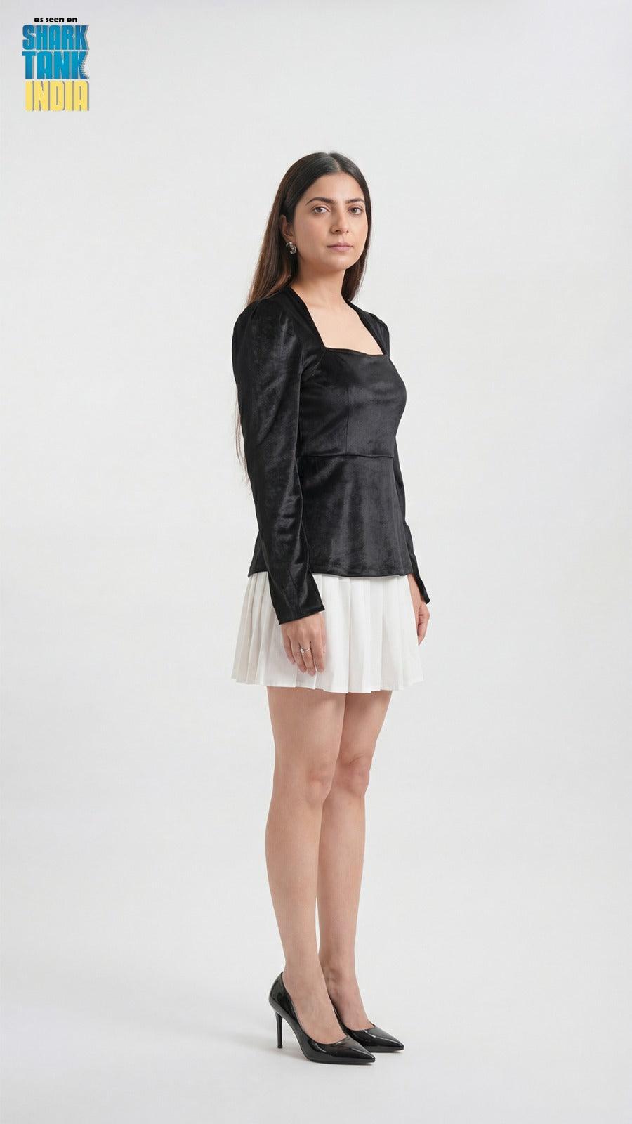 Woman wearing a black blazer, black top, and white skirt on a white background