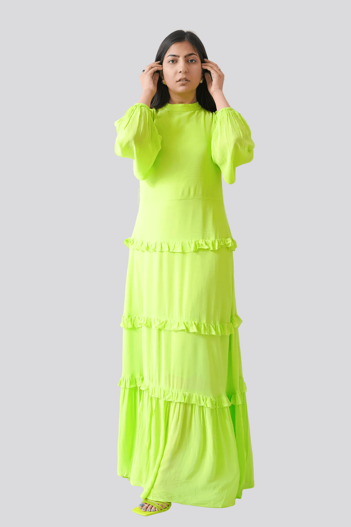 Woman wearing a bright green dress standing indoors with a plant in the background