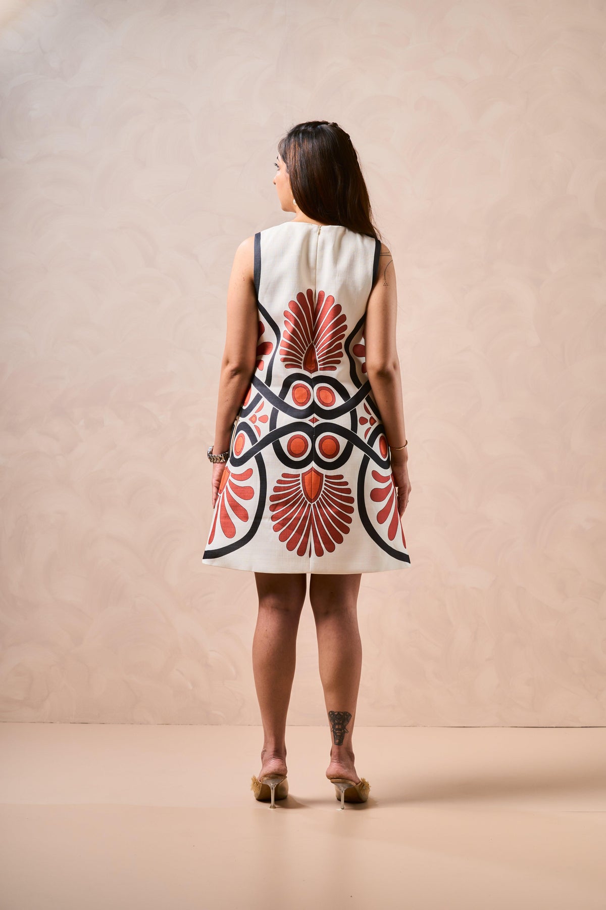 Woman wearing a sleeveless dress with a red and black abstract pattern on a beige background