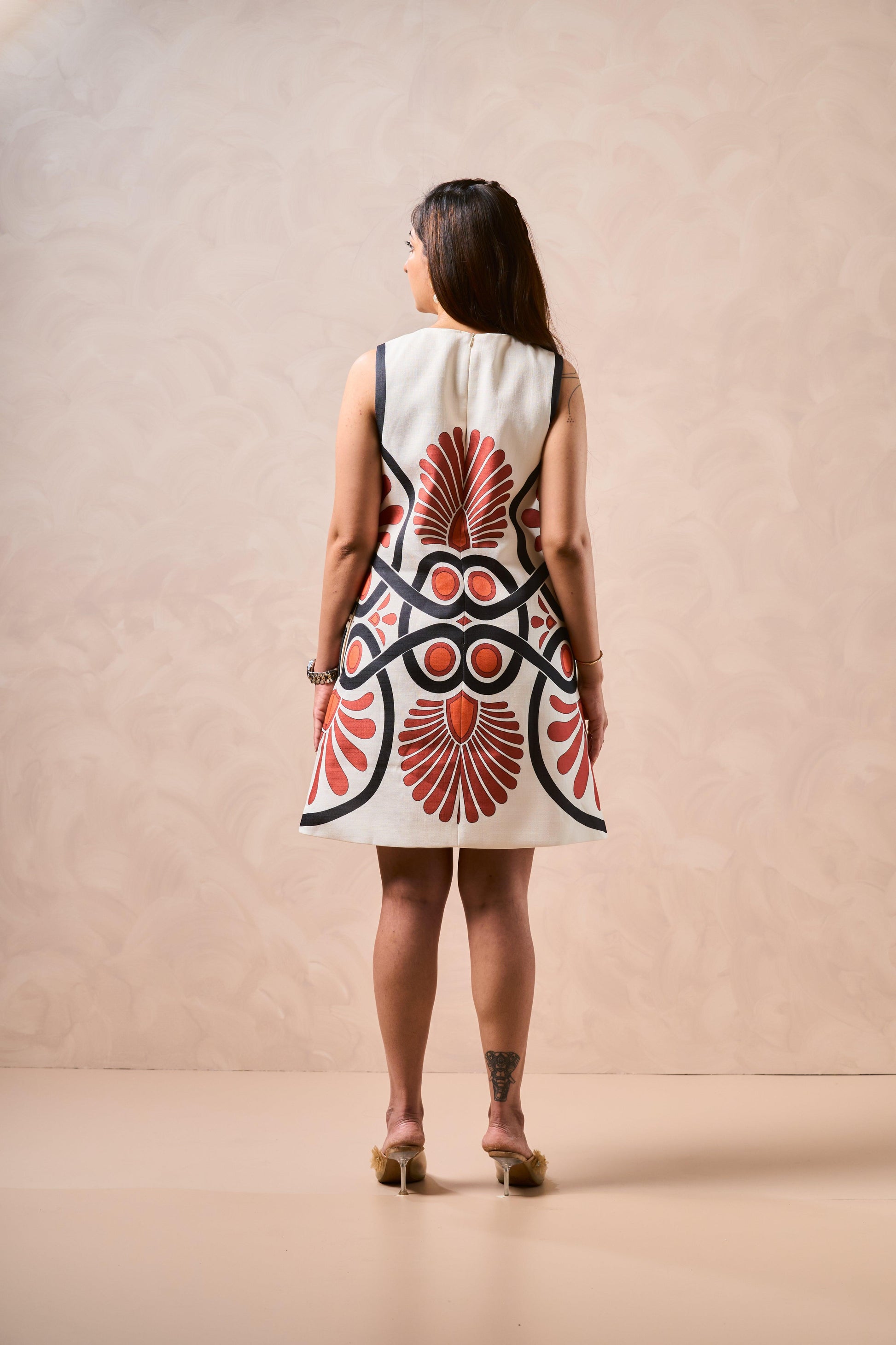 Woman wearing a sleeveless dress with a red and black abstract pattern on a beige background