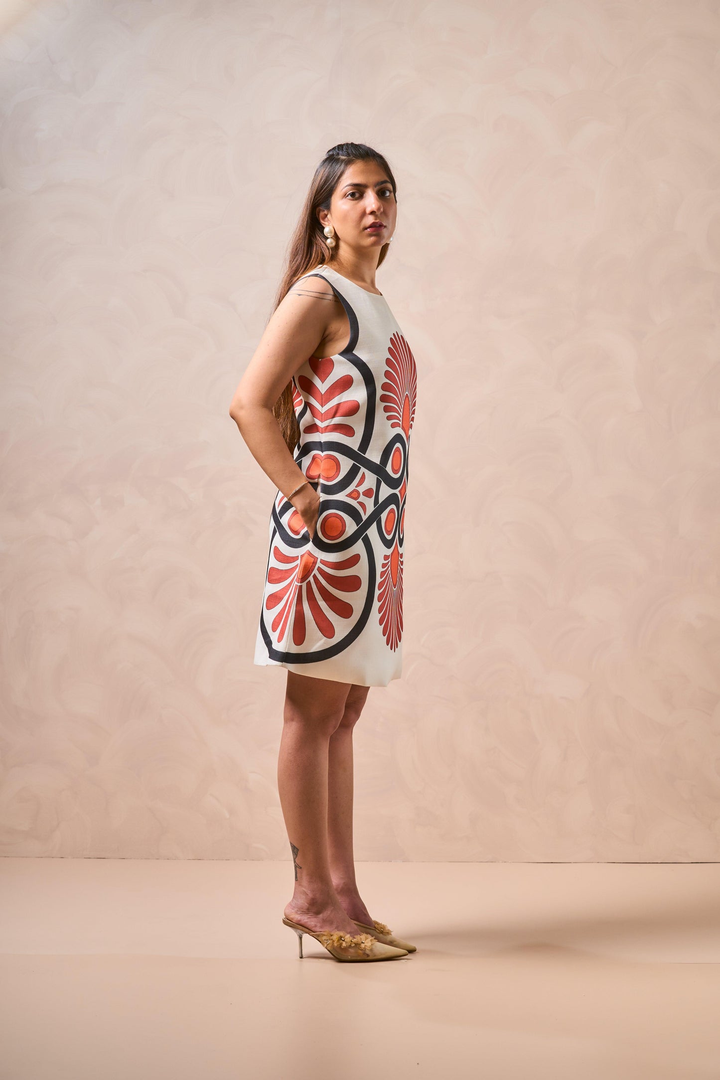 Woman wearing a sleeveless dress with a red and black pattern on a beige background