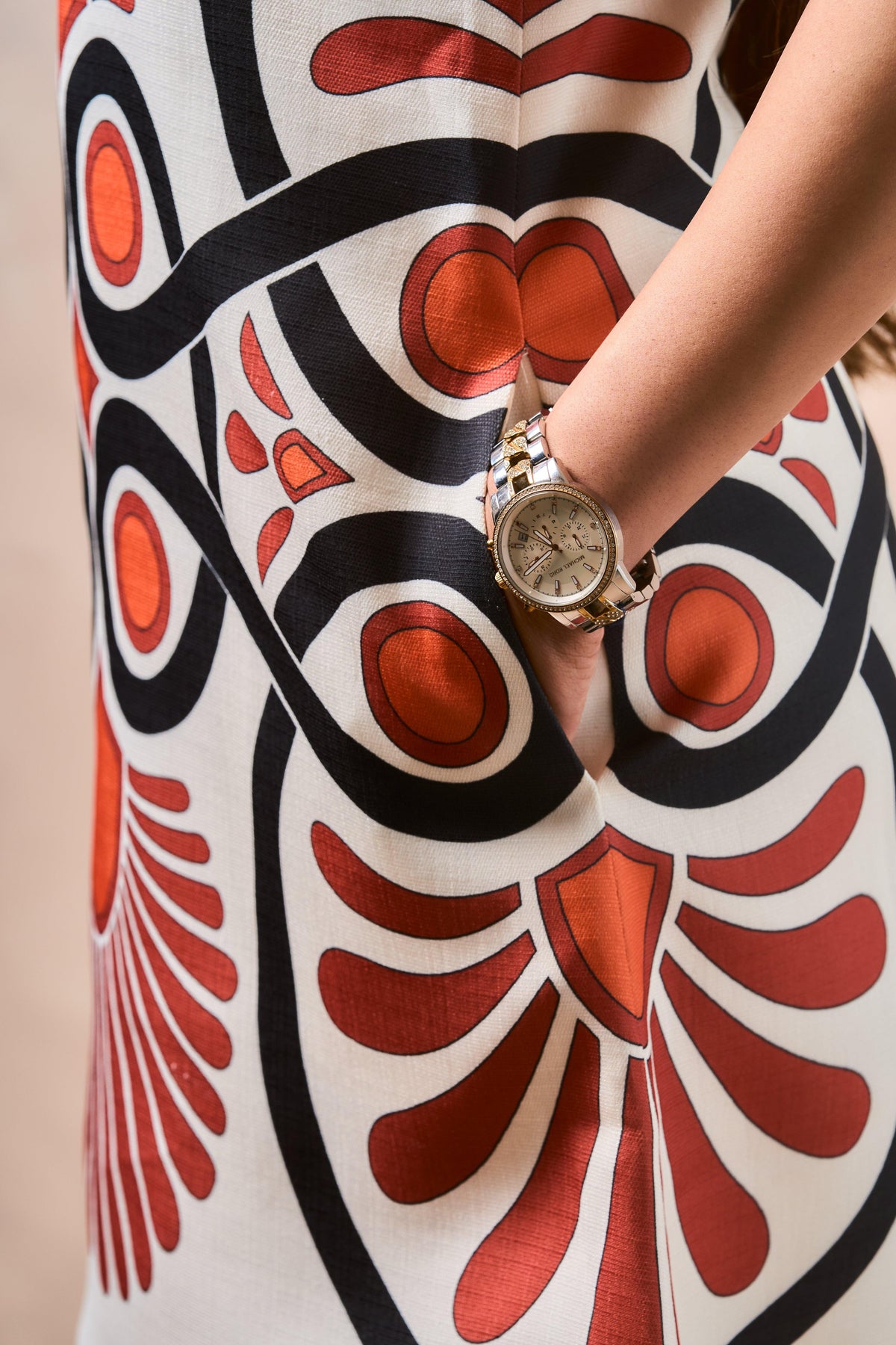 Person wearing a watch on a sleeveless dress with a red and black abstract pattern.