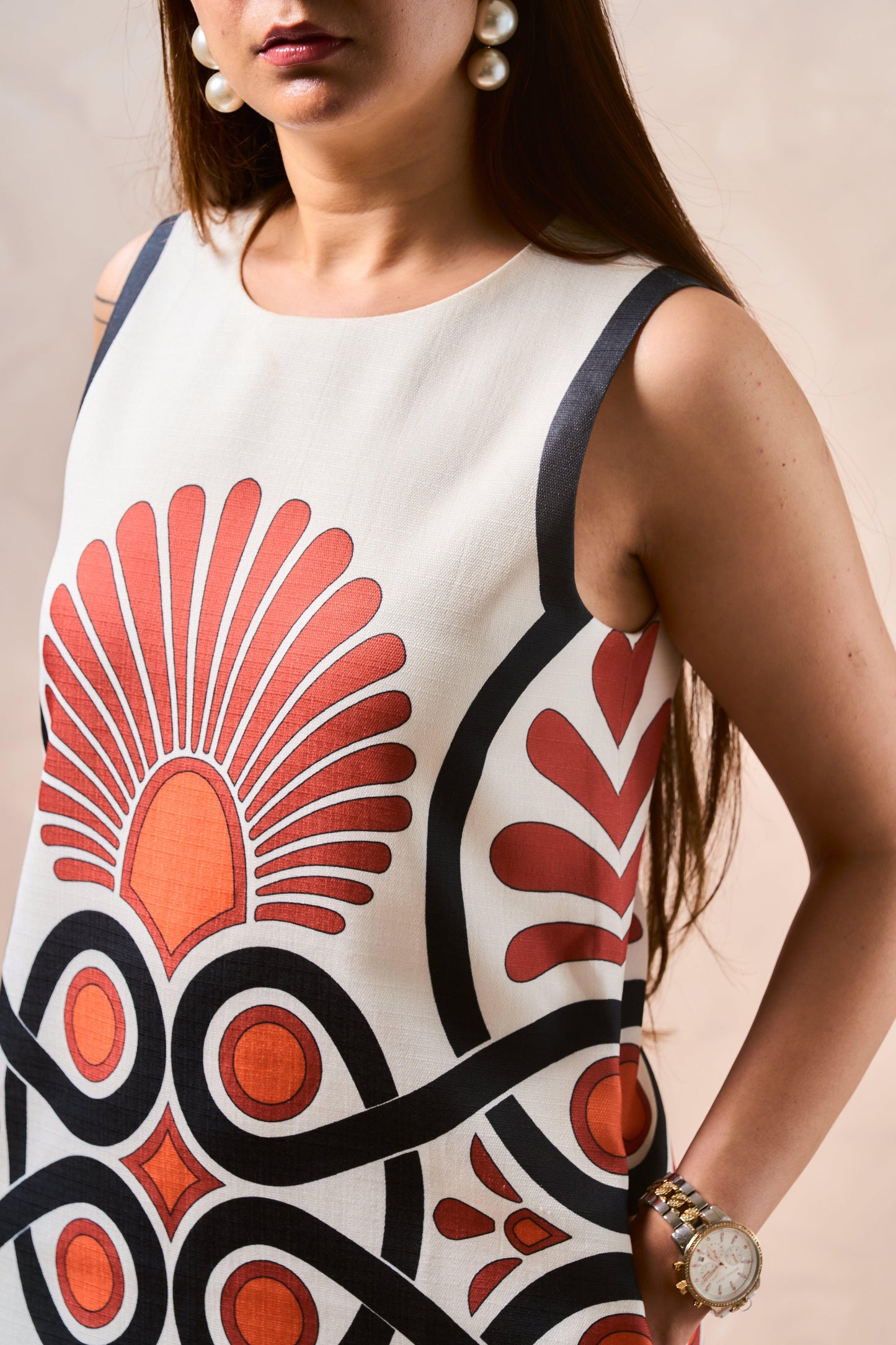 Person wearing a sleeveless dress with a red and black abstract pattern on a beige background