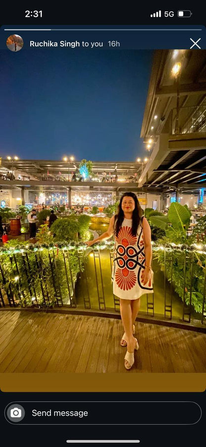 Woman in a colorful dress standing on a rooftop at night with lights and people in the background
