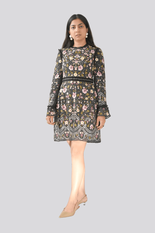 Woman wearing a floral dress standing in front of a plant against a white wall.