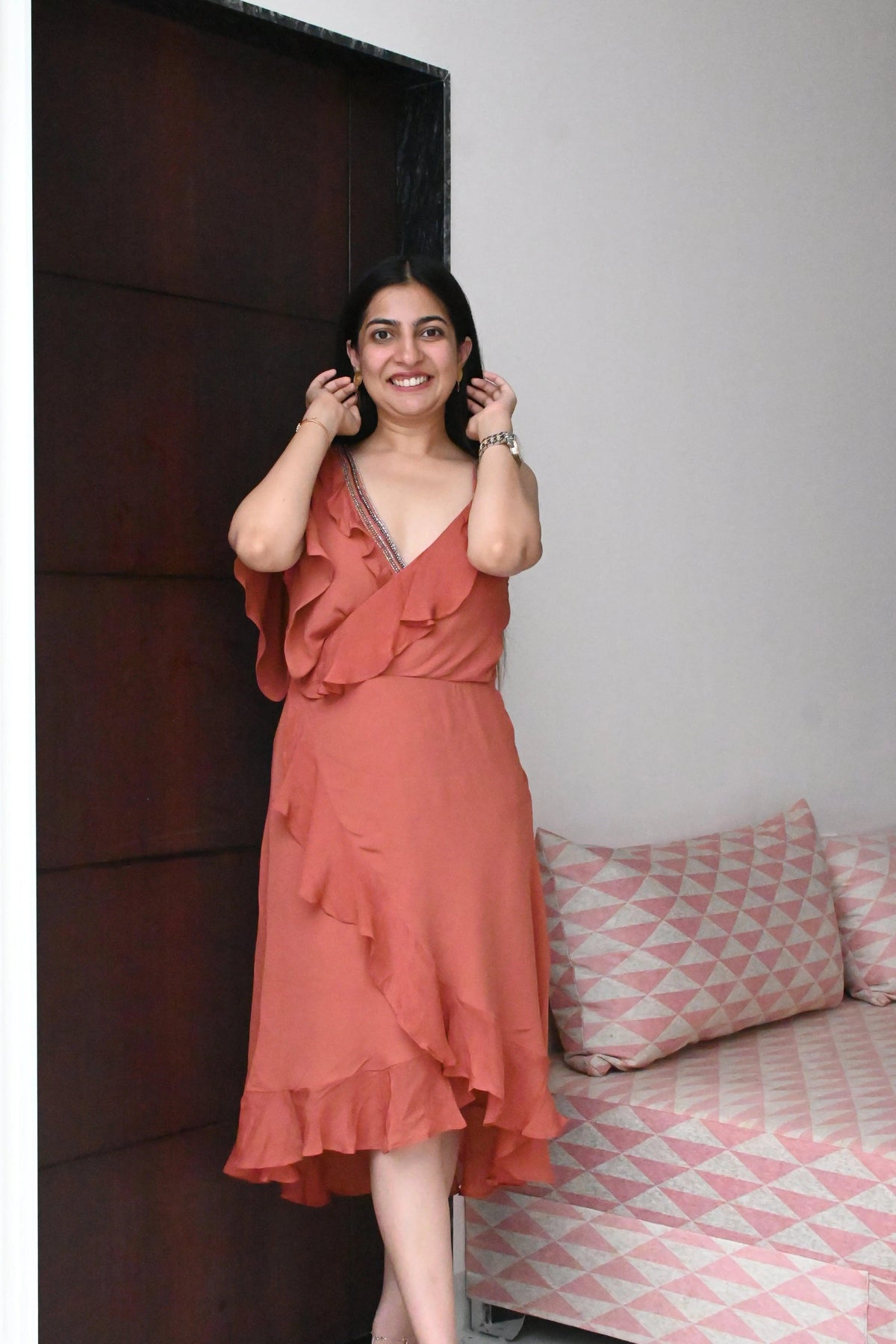 Woman in a red dress standing in a room with a bed and pillows.