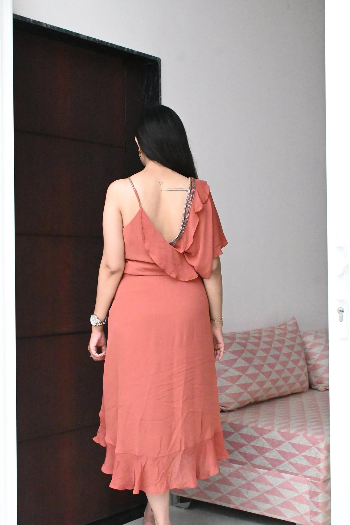 Woman in a coral dress standing in a room with a bed and pillows.