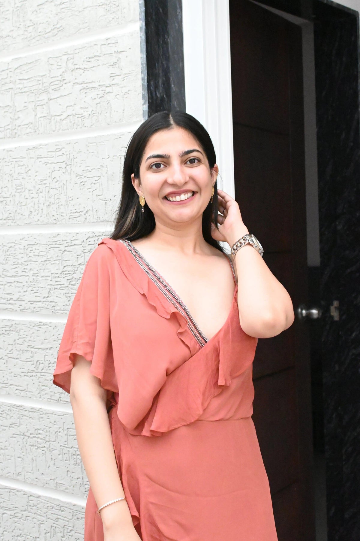 Woman in a coral dress standing against a white wall and dark door.