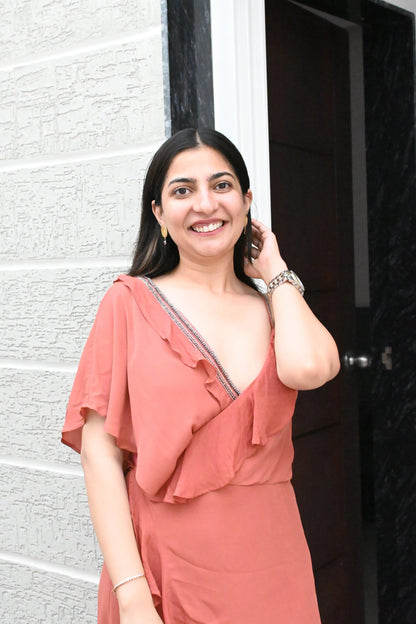 Woman in a coral dress standing against a white wall and dark door.