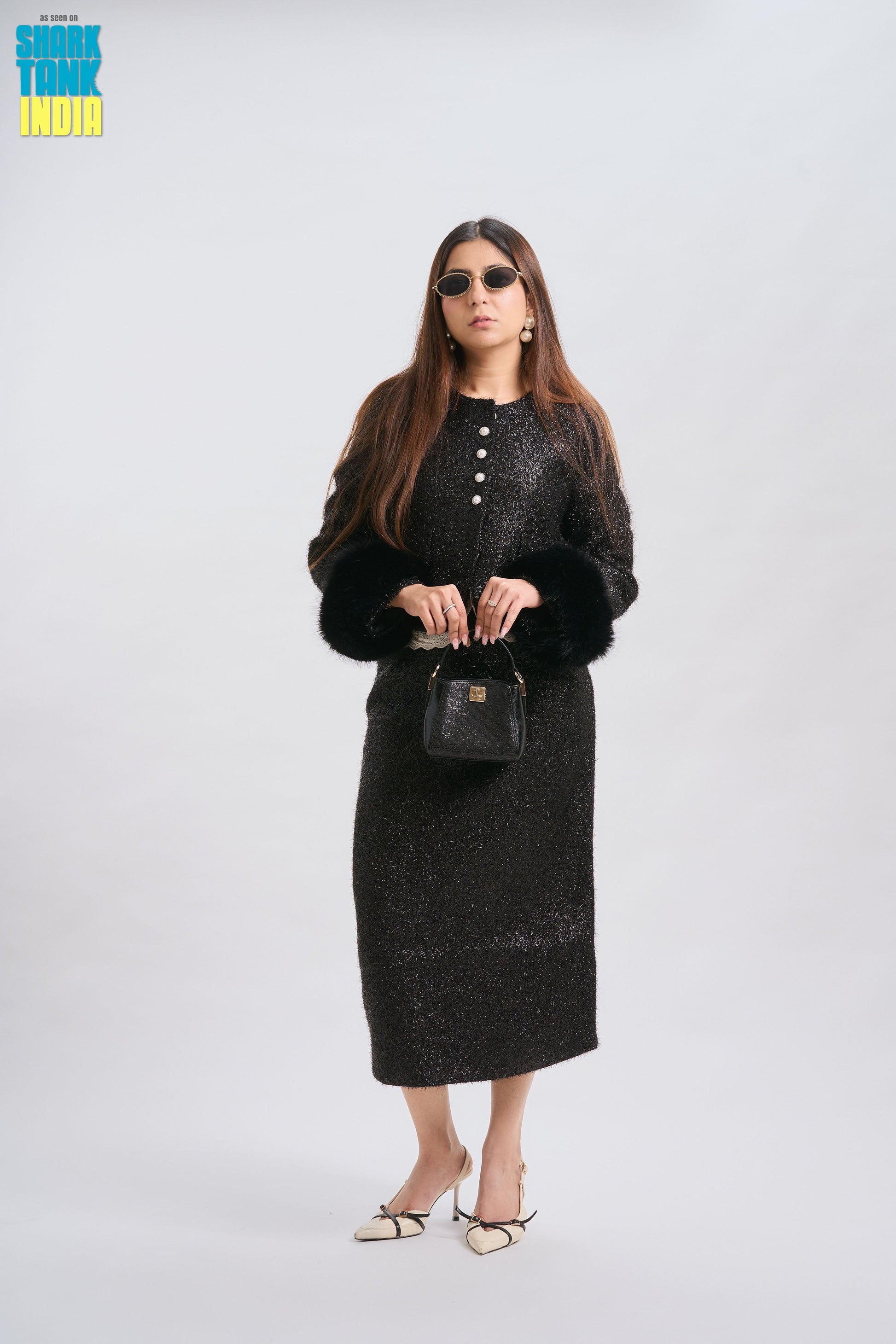 Woman wearing a black outfit with sunglasses and holding a handbag on a white background