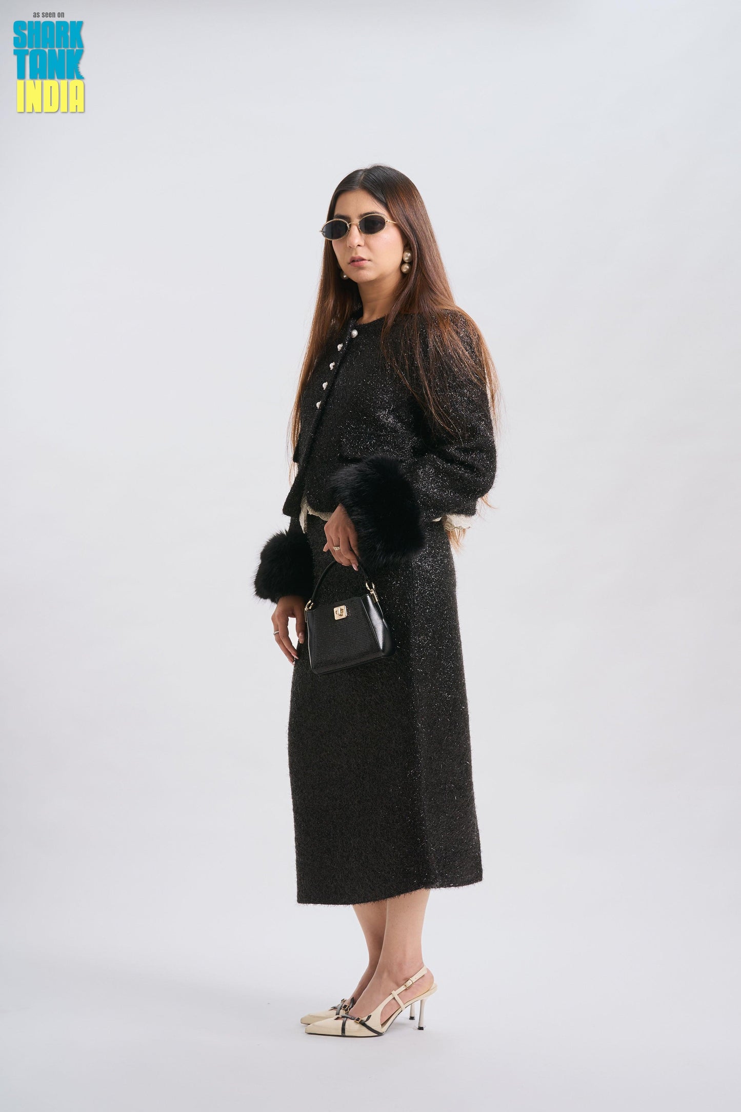 Woman in a black outfit with sunglasses and a handbag on a white background