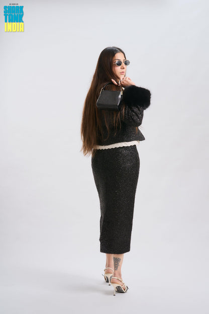 Woman in a black outfit with fur accents holding a handbag on a white background