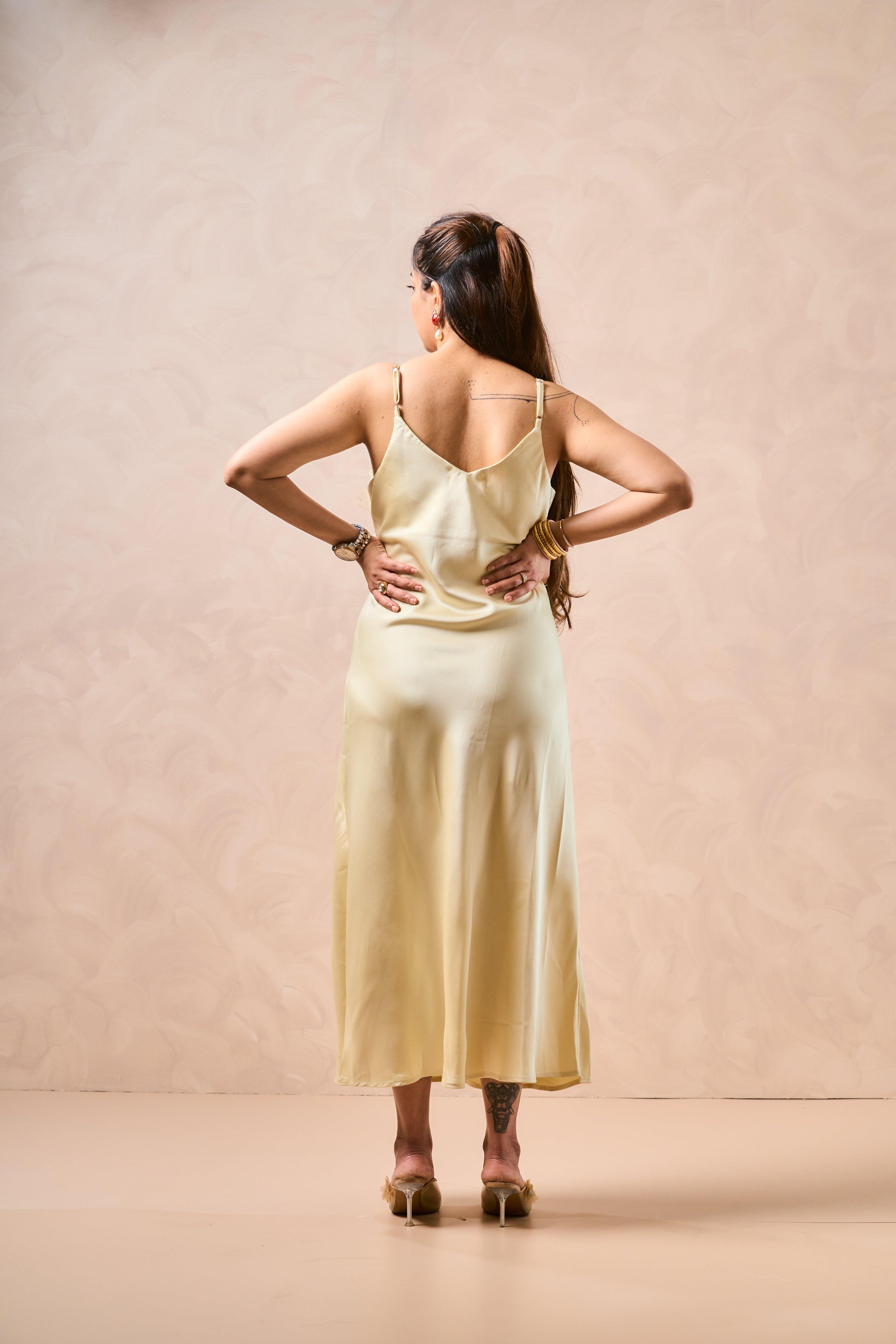 Woman wearing a light yellow satin slip dress against a beige background