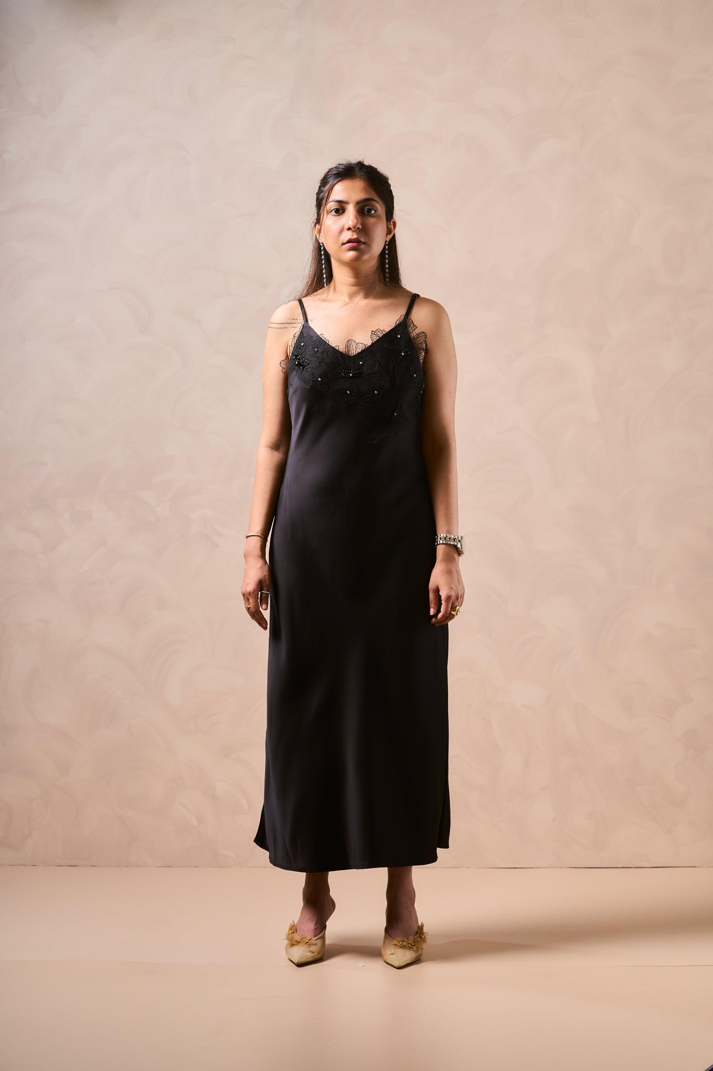 Woman wearing a black slip dress with embellishments against a beige background