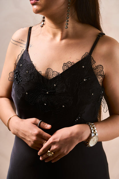 Woman wearing a black lace dress with intricate detailing on a neutral background
