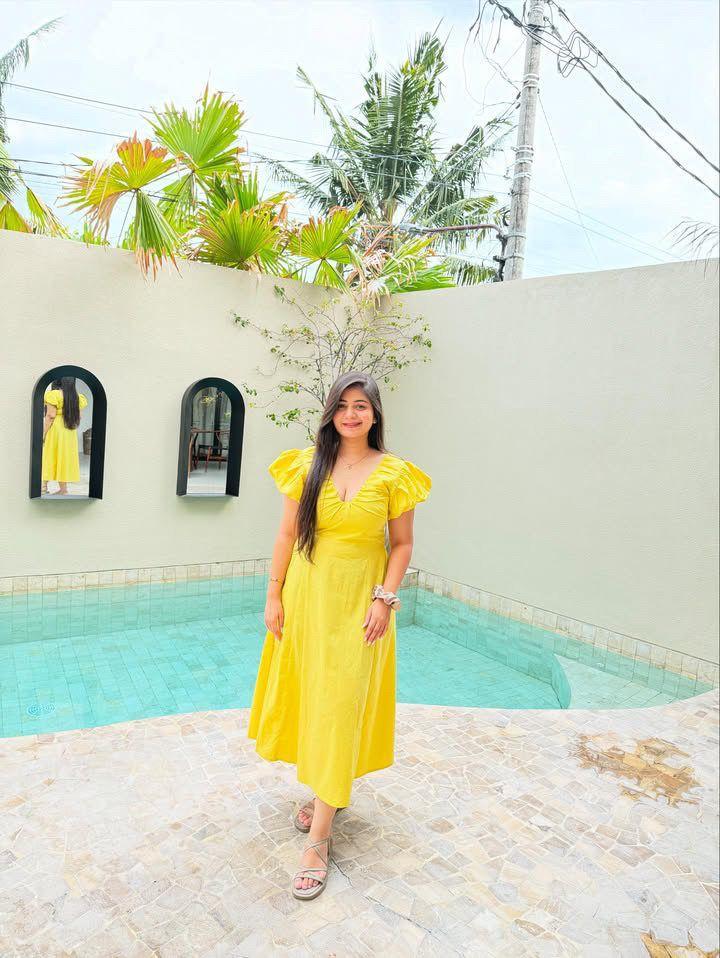 Woman in a yellow dress standing by a pool with palm trees in the background