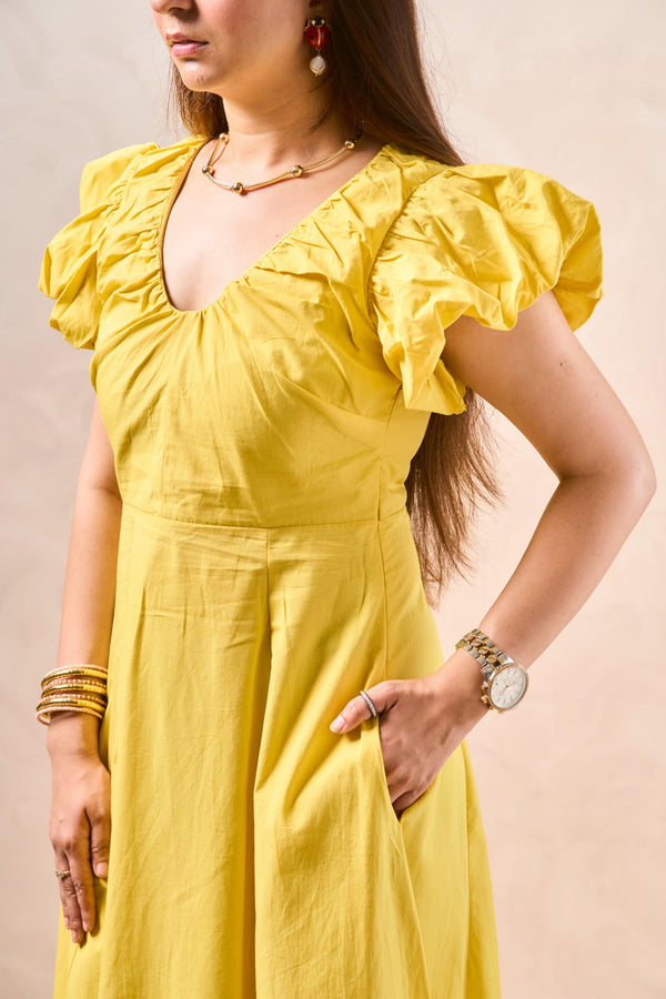Woman wearing a yellow dress with ruffled sleeves against a beige background