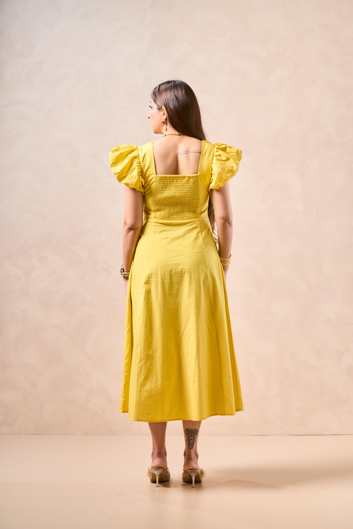 Woman wearing a yellow dress with ruffled sleeves against a beige background