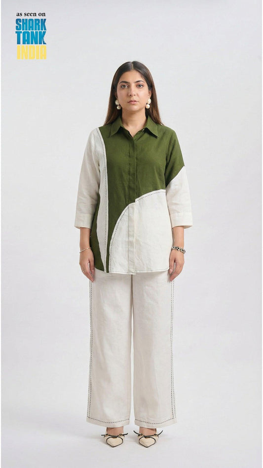 Woman wearing a green and beige color-blocked shirt with white pants on a white background.