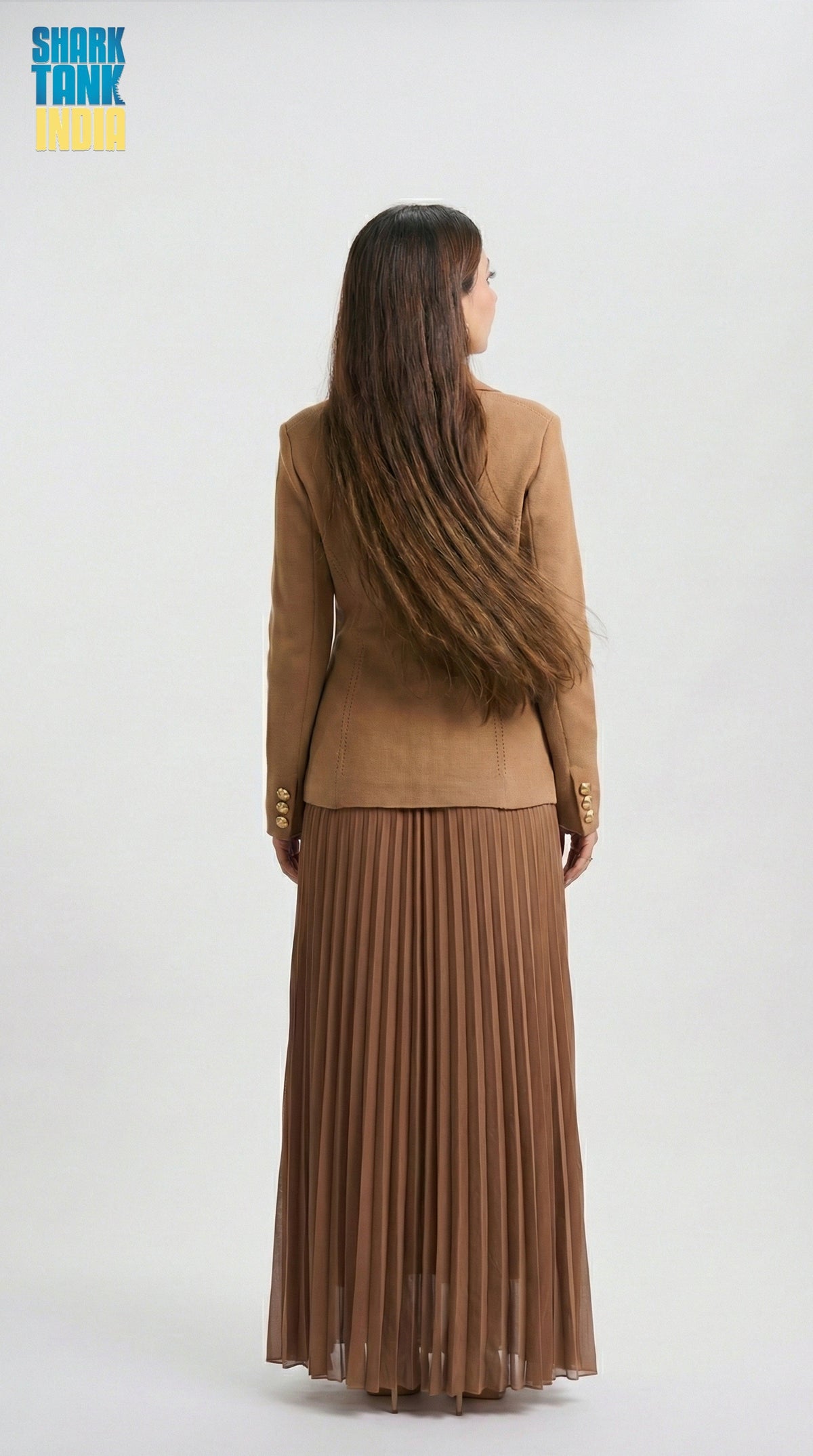 Person wearing a brown suit with a pleated skirt on a white background