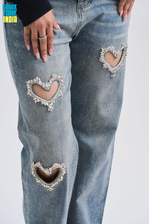 Blue jeans with heart-shaped cutouts and embellishments on a white background