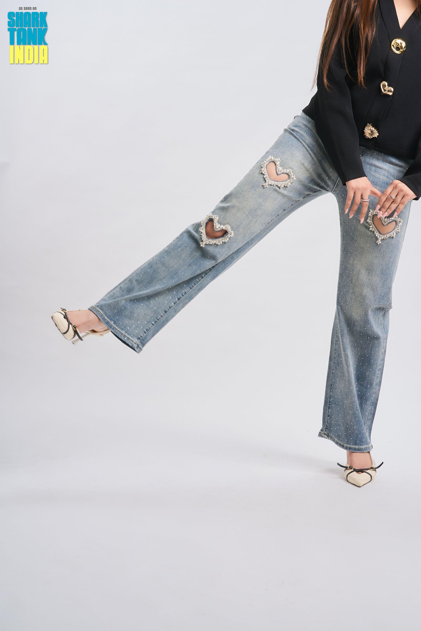 Person wearing a black top with gold buttons and ripped blue jeans on a white background