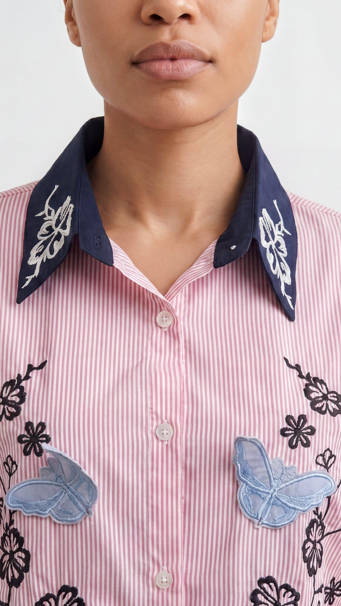 Close-up of a person wearing a pink striped shirt with decorative patches on a white background