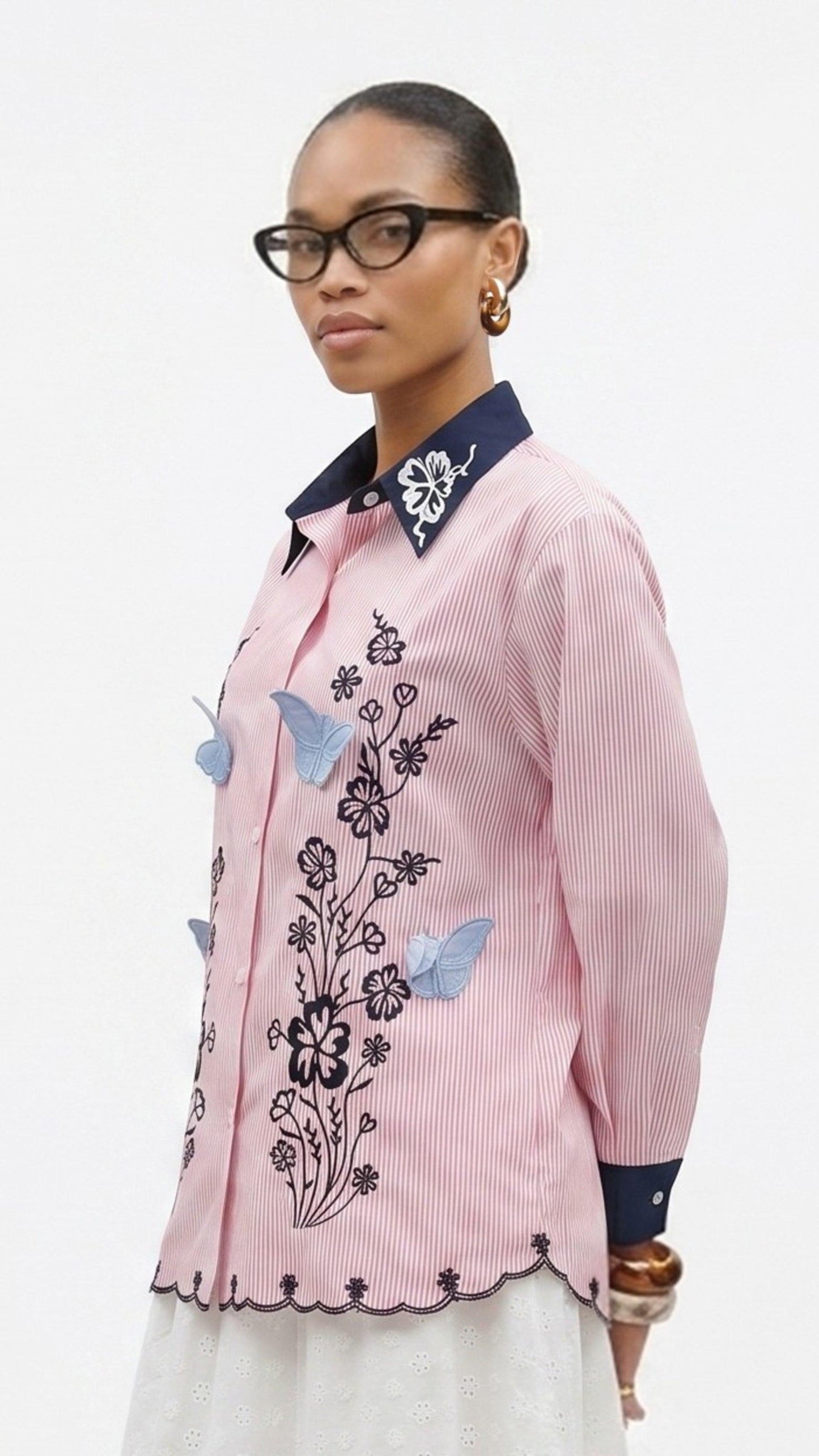 Woman wearing a pink embroidered shirt with blue butterflies on a white background