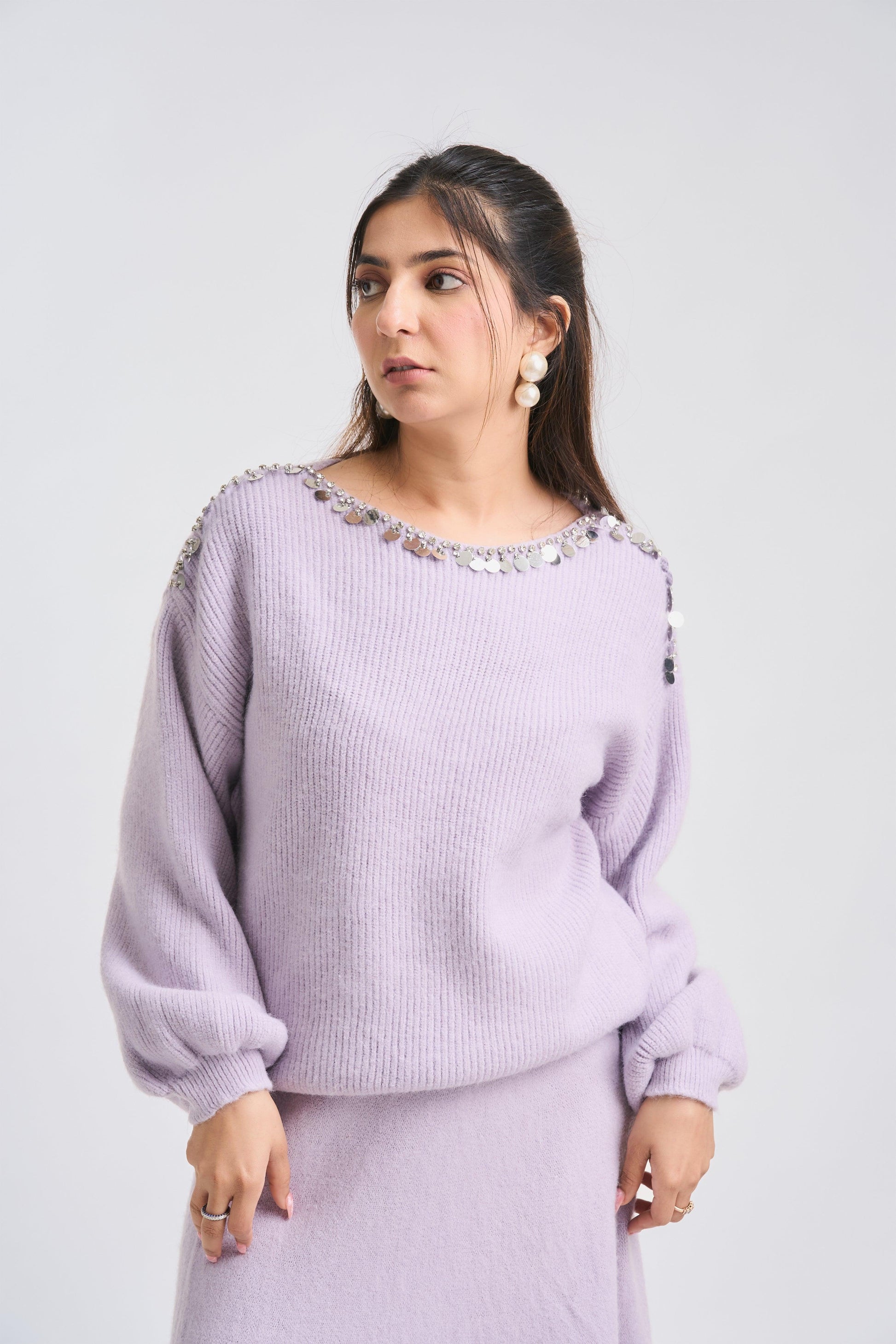 Woman wearing a light purple sweater with decorative elements on a plain background