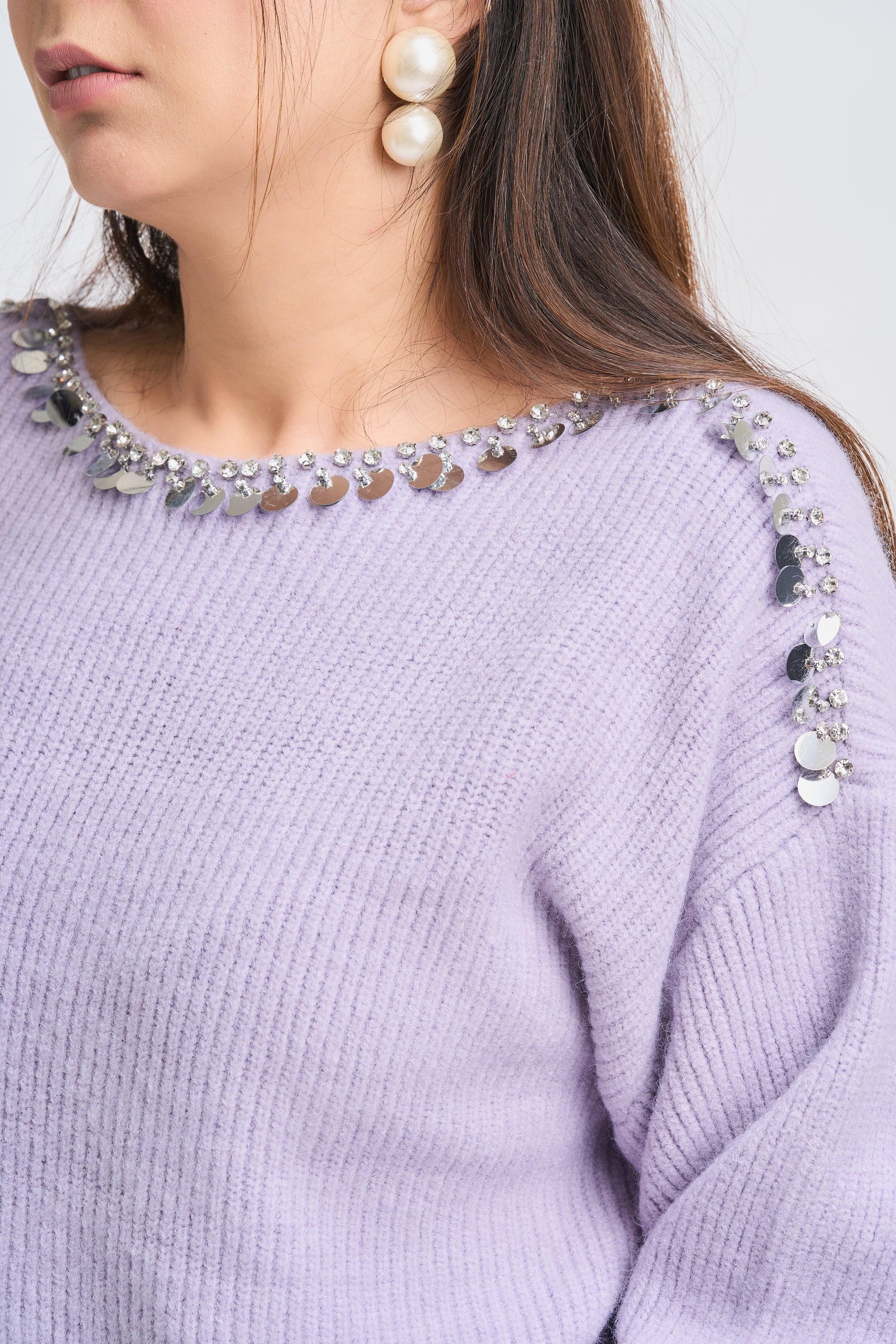 Close-up of a person wearing a light purple sweater with decorative embellishments.