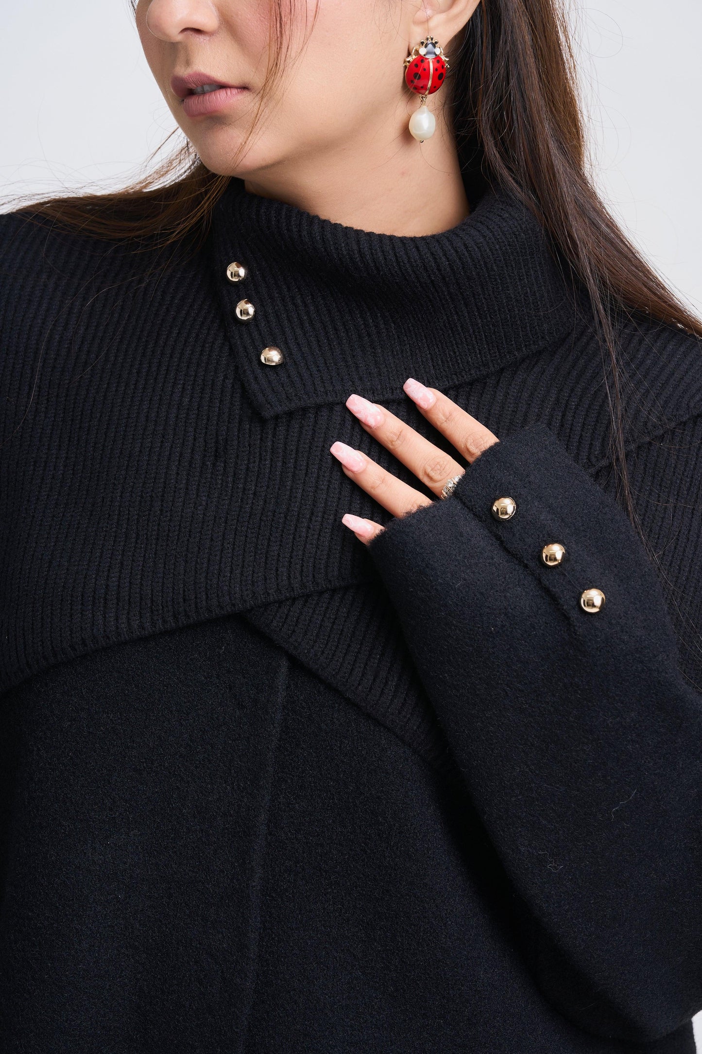 Close-up of a person wearing a black coat with gold buttons, red earrings, and a ring.