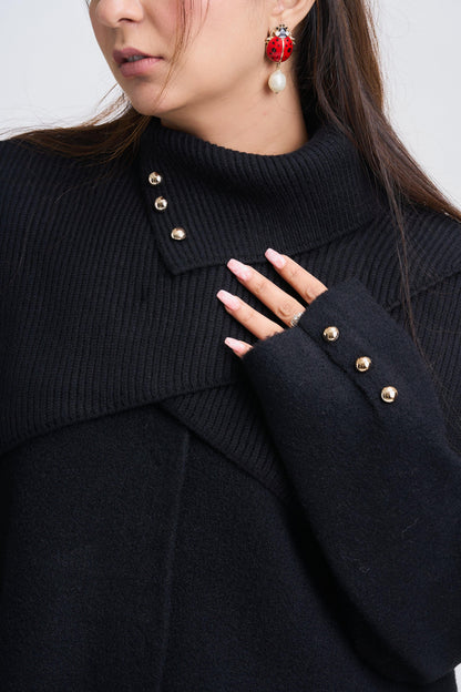 Close-up of a person wearing a black coat with gold buttons, red earrings, and a ring.