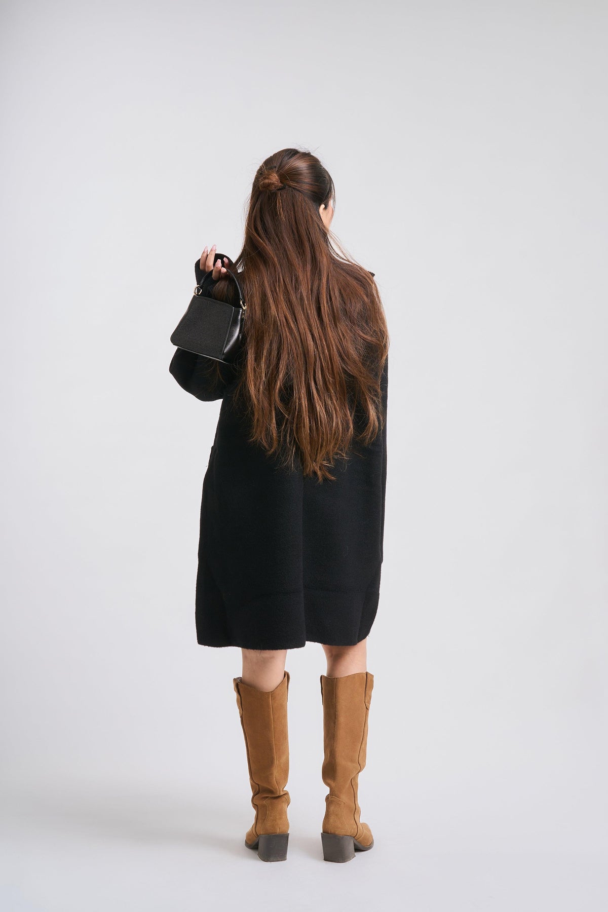 Person wearing a black coat and brown boots on a white background